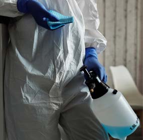 Healthcare professional holding a cleaning agent and wearing protective garbs.